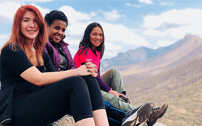 Three people sitting on top of a boulder smiling